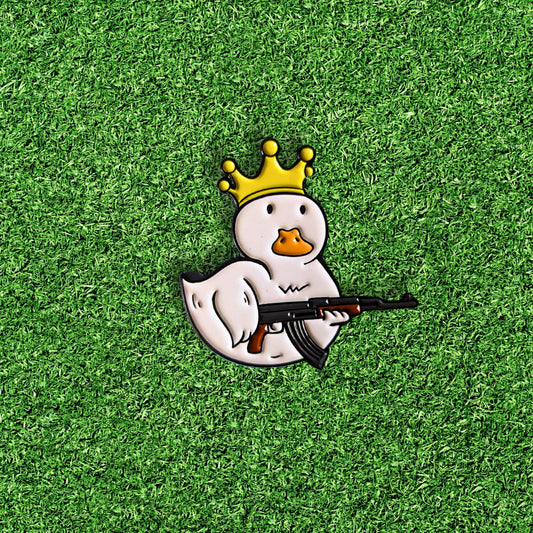 golf ball marker of a white duck wearing a gold crown and holding a gun