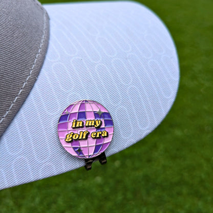 purple mirrorball golf ball marker that says 'in my golf era' clipped on hat